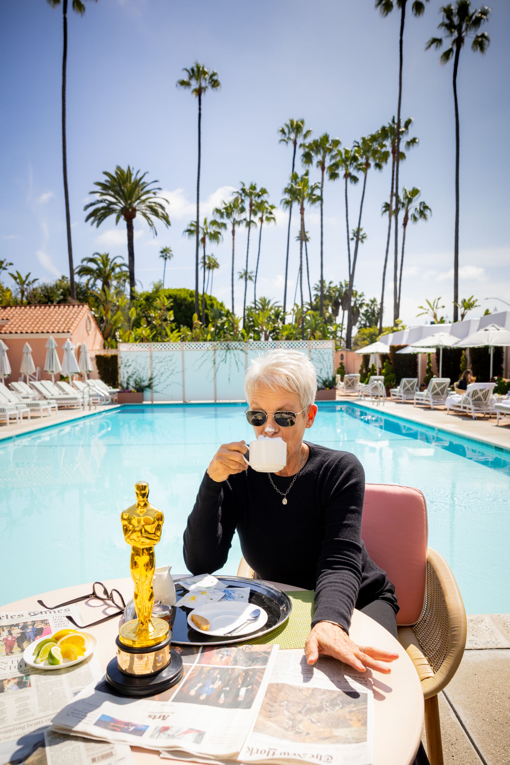 A woman in sunglasses sips from a cup, with her Oscar at her side and a dab of latte foam on her nose.