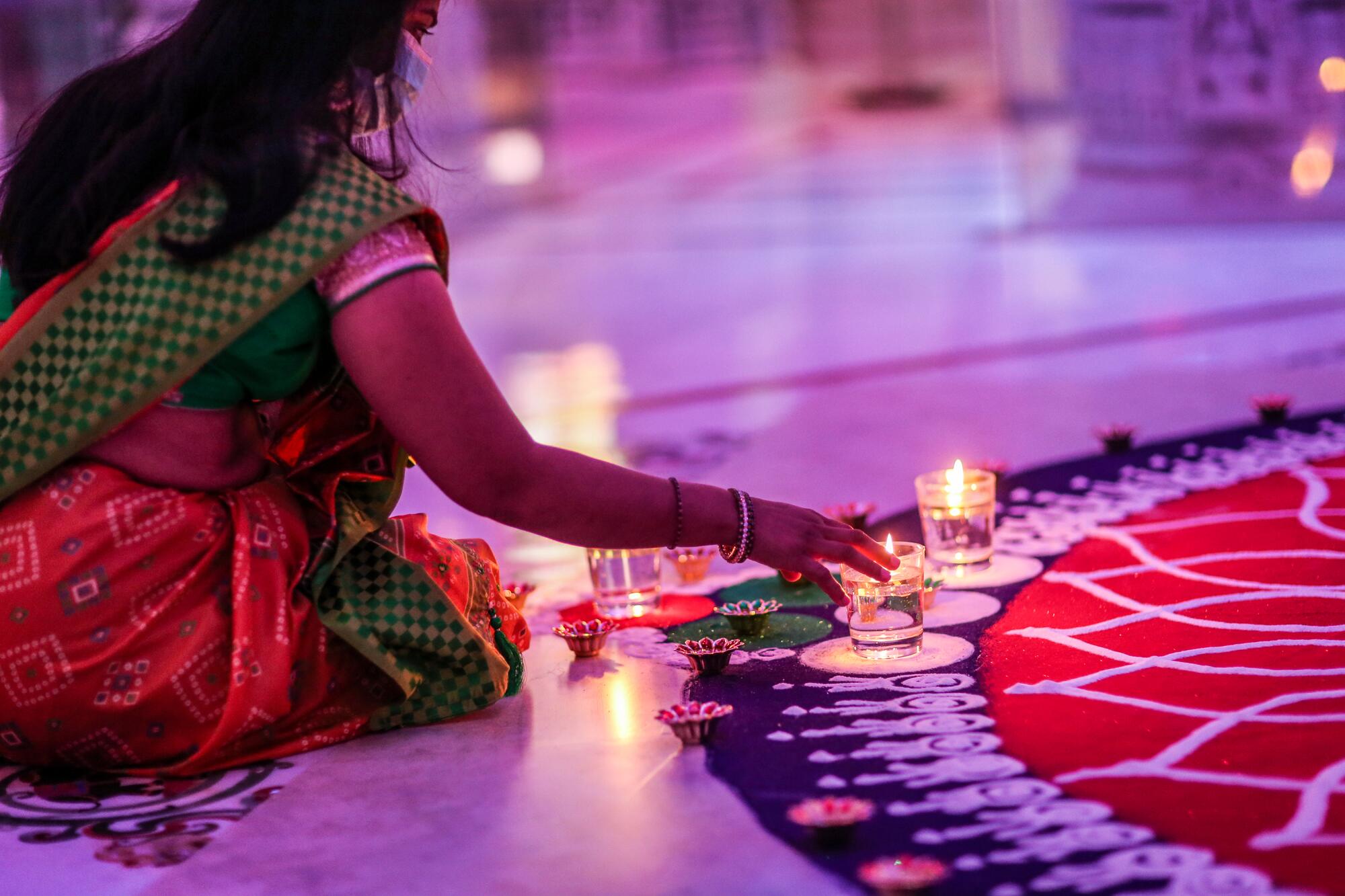 A woman kneels and places a candle on the edge of an intricate work of sand art inside a Hindu temple
