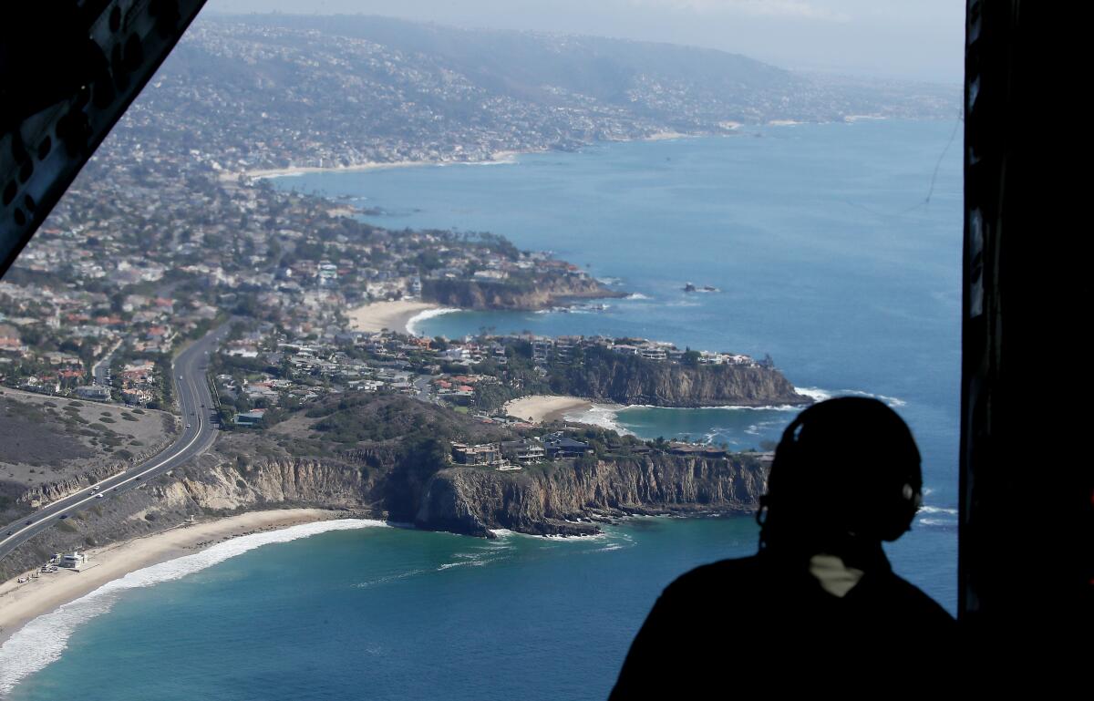 A Coast Guard member looks out of an airplane at Laguna Beach.