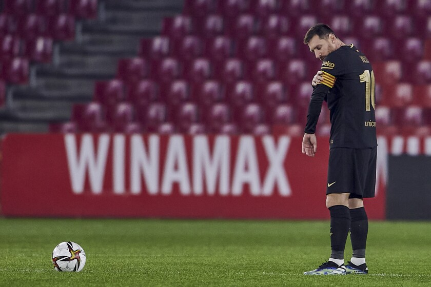 Lionel Messi stands on the field near a soccer ball.