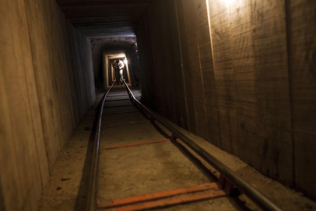 Metal tracks for rail cars descend into a lighted, wood-paneled tunnel as a man makes his way toward the camera