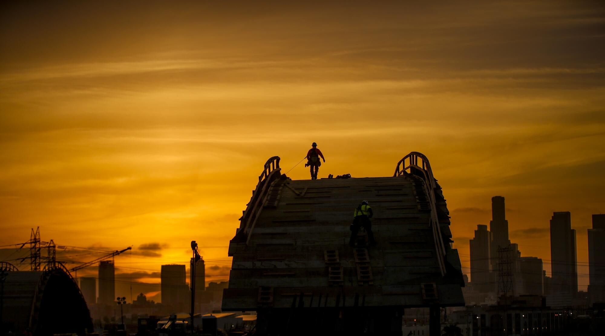 A worker walking at the top of an arch is silhouetted by the setting sun 