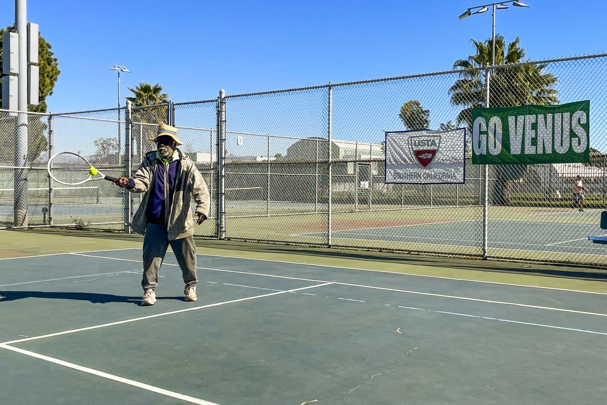 A man hits a tennis ball in front of a sign that says "Go Venus."