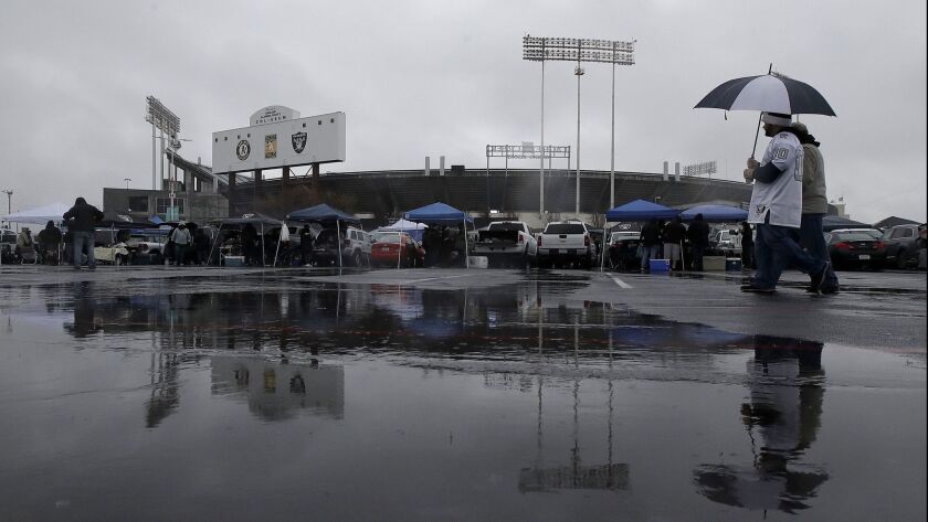 Fans brave the rain prior to the start of the Raiders-Broncos game Monday at Oakland-Alameda County Coliseum. A police SUV was stolen during the game.