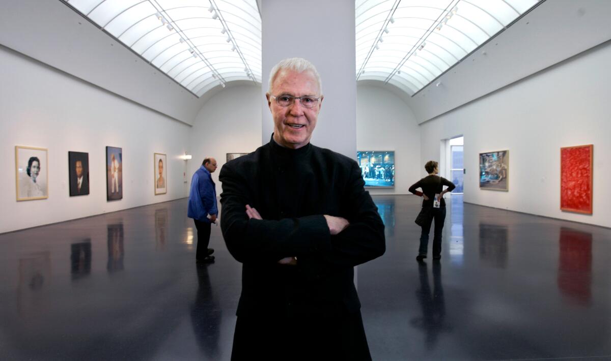 Robert Fitzpatrick stands in an art gallery with arms folded, in a black coat.