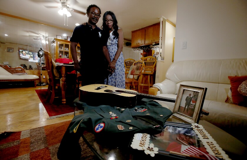 Two people look at a guitar, uniform and pictures on a table.