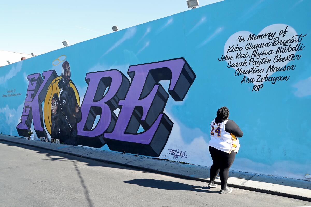 A fan stands in front of a Kobe mural painted on the side of El Toro Bravo market in Costa Mesa.