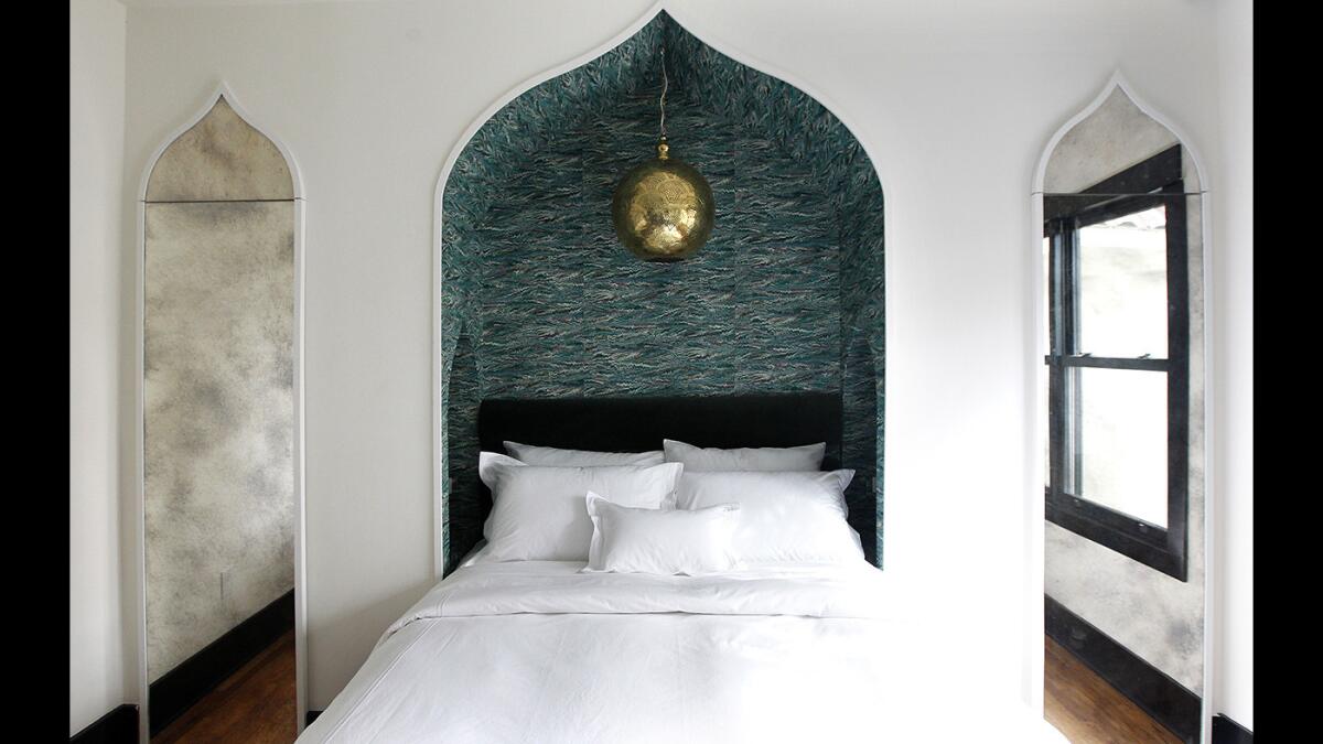 A bedroom in Hotel Covell's Chapter 4 two-bedroom suite features onion dome-shaped niches and handmade marbled wallpaper inspired by George Covell's fictional travels in Morocco and India. The mirrored surfaces that flank the inset bed contain closets.