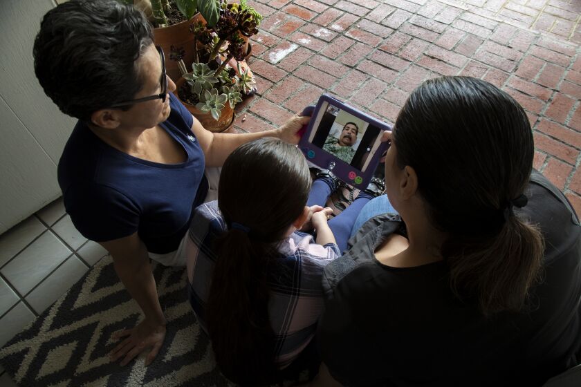 MONTEBELLO, CA - SEPTEMBER 14, 2020: Teresa Gonzalez, left, with her granddaughter Camila, 8, and daughter Mabel, FaceTime with Gonzalez's husband Francisco while he recuperates from the coronavirus in a nearby skilled nursing facility on September 14, 2020 in Montebello, California. Francisco was hospitalized July 13 and remained there for 51 days. During that time the family was unable to hold onto their liquor store in Los Angeles.(Gina Ferazzi / Los Angeles Times)