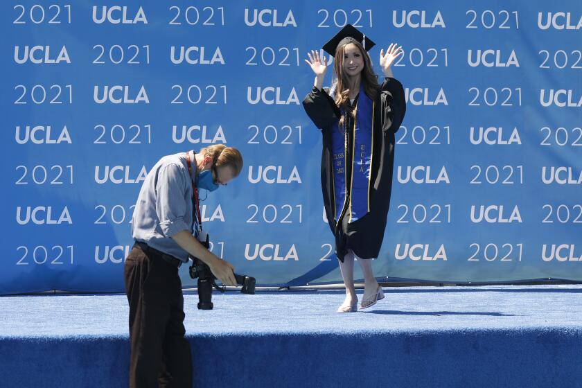 LOS ANGELES, CA - JUNE 10: Graduating with a degree in Communication Studies and Business/Economics, Maddie Park waves to her parents Richard and Stephanie Park as graduating UCLA students walk the stage in Drake Stadium while their names are announced with their image on a video monitor and pose for official photographs as they take part in a "Graduation Celebration." Up to 230 students per hour will participate in the graduate procession through Drake Stadium each day for six days with up to one student every 15 seconds. More than 9,000 students over six days starting Thursday before and after a virtual ceremony on Friday night, will walk through Drake Stadium with up to two guests to get the graduation experience of crossing a real stage as their names are read. Roughly 14,000 undergraduates and graduate students total are expected to receive their degrees from UCLA this year. UCLA on Thursday, June 10, 2021 in Los Angeles, CA. (Al Seib / Los Angeles Times).