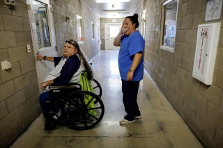 A woman in a wheelchair sits in front of a door as a woman stands behind her in a hallway