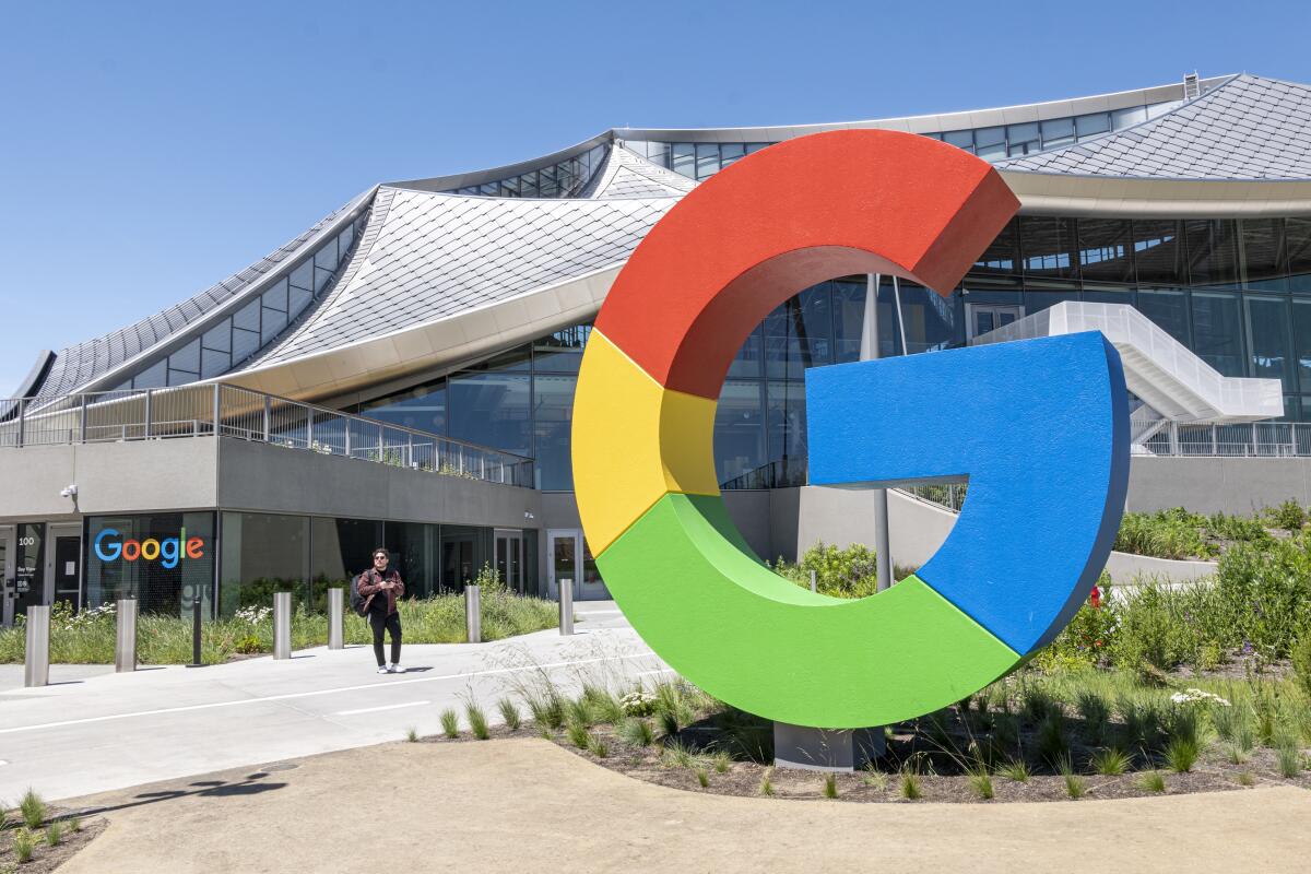 A large G sign in front of a building with the word Google on a window.