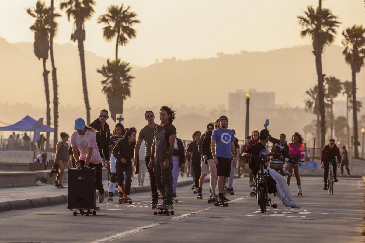 A group of mostly skateboarders ride along the boardwalk in Santa Monica. 