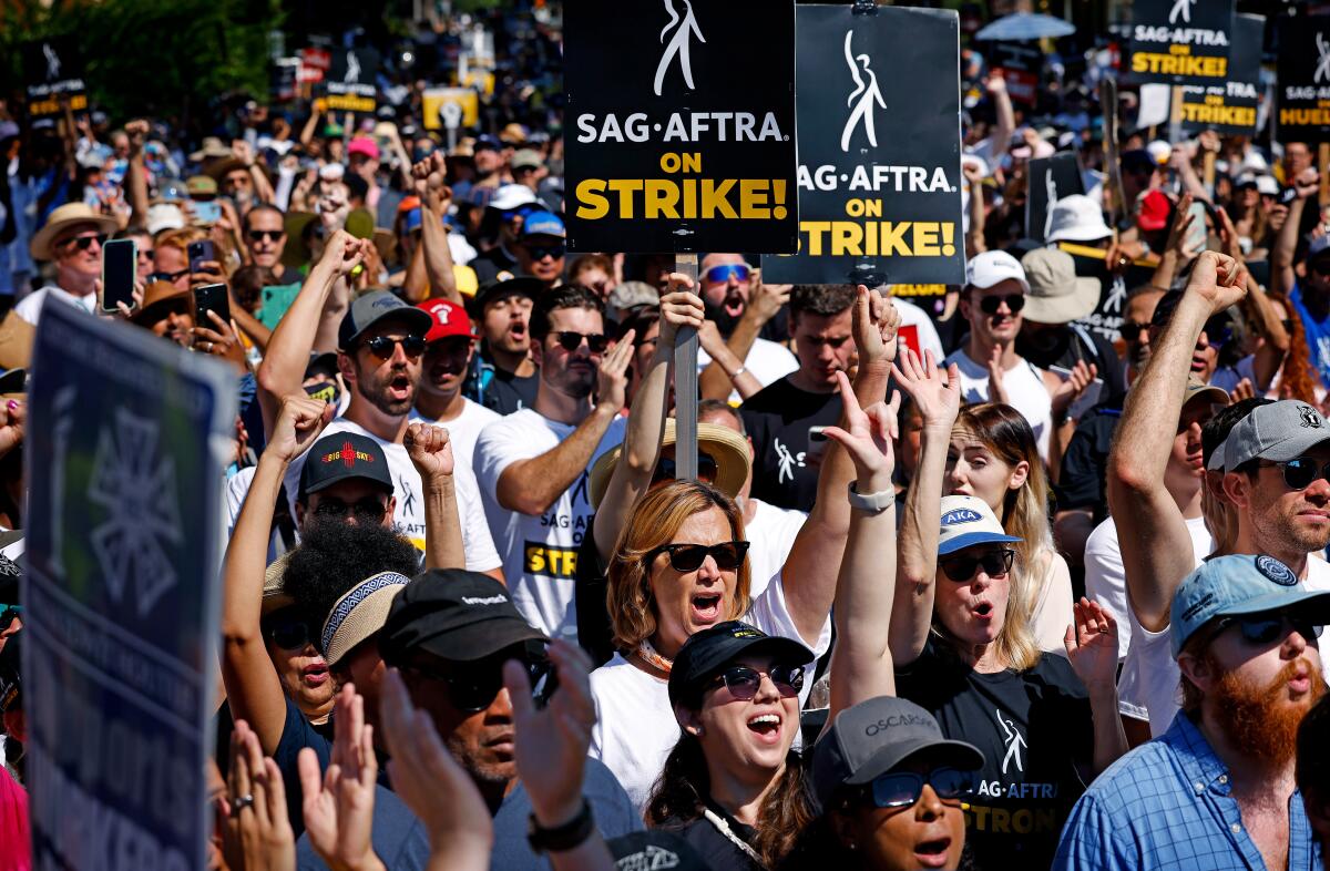 A large crowd of people shouting and holding picket signs that read "SAG-AFTRA on Strike!"