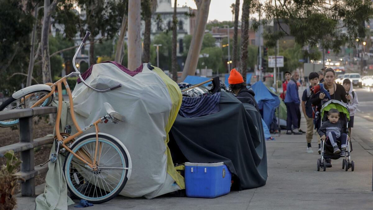 Pedestrians share the sidewalk along Arcadia Street with homeless camps in downtown Los Angeles.