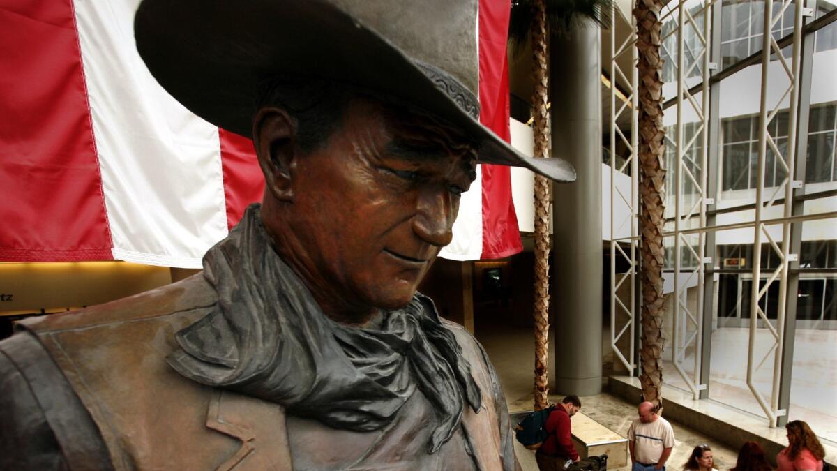 A bronze statue of John Wayne in a western hat and scarf 