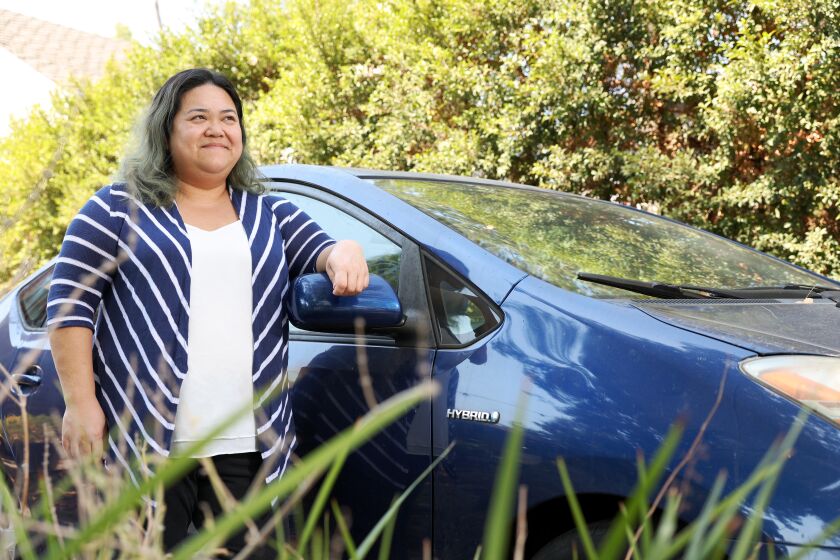 Los Angeles, CA - September 06: Nam Trinh stands for a portrait with her 2008 Prius that had its catalytic converter stolen four times over a span of six months at her house on Tuesday, Sept. 6, 2022 in Los Angeles, CA. It was stolen twice from outside her home in Eagle Rock; once in Sacramento; and once in Las Vegas, while parked in the garage at the MGM Grand. (Dania Maxwell / Los Angeles Times)