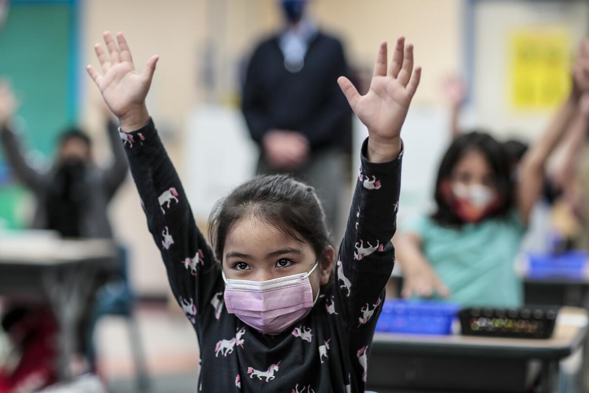 A kindergarten girls wearing  pink mask raises both hands in class. 