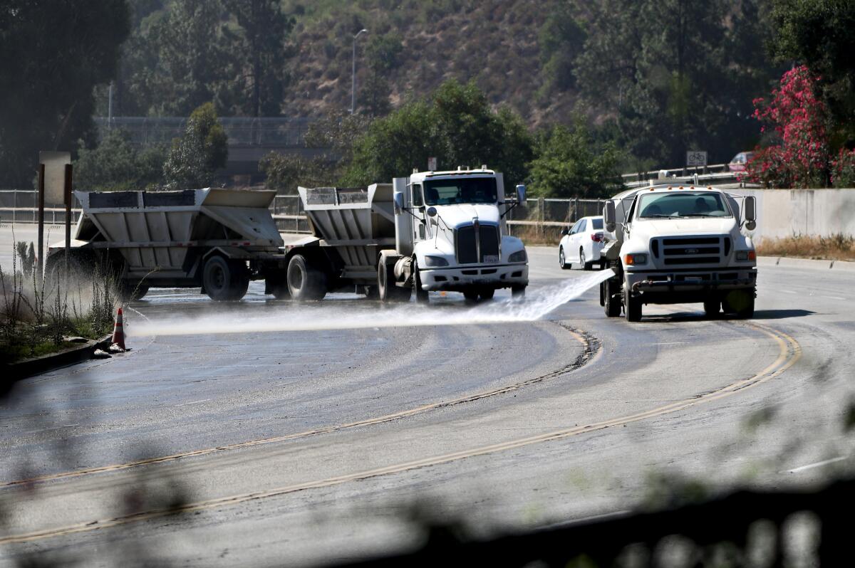 A water truck washes down Oak Grove Drive as a hauler exits out with a load of dirt from the Hahamongna Watershed Park L.A. County Public Works Department's Devil's Gate Dam Sediment Removal project. Their route will be shifted during peak traffic hours near La Cañada High, according to the LCUSD superintendent.