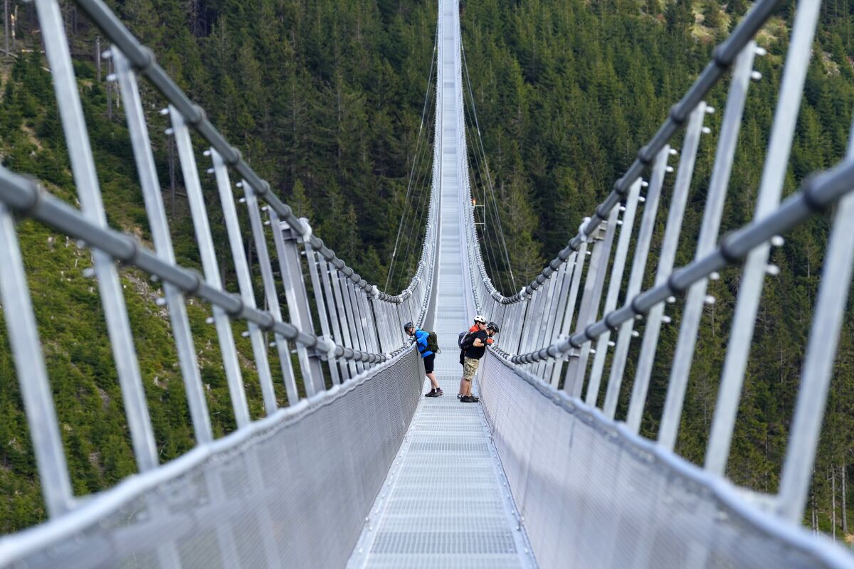 People stand on a suspension bridge for the pedestrians that is the longest such construction in the world a day before its official opening at a mountain resort in Dolni Morava, Czech Republic, Thursday, May 12, 2022. The 721-meter (2,365 feet) long bridge is built at the altitude of more than 1,100 meters above the sea level. It connects two ridges of the mountains up to 95 meters above a valley between them. (AP Photo/Petr David Josek)