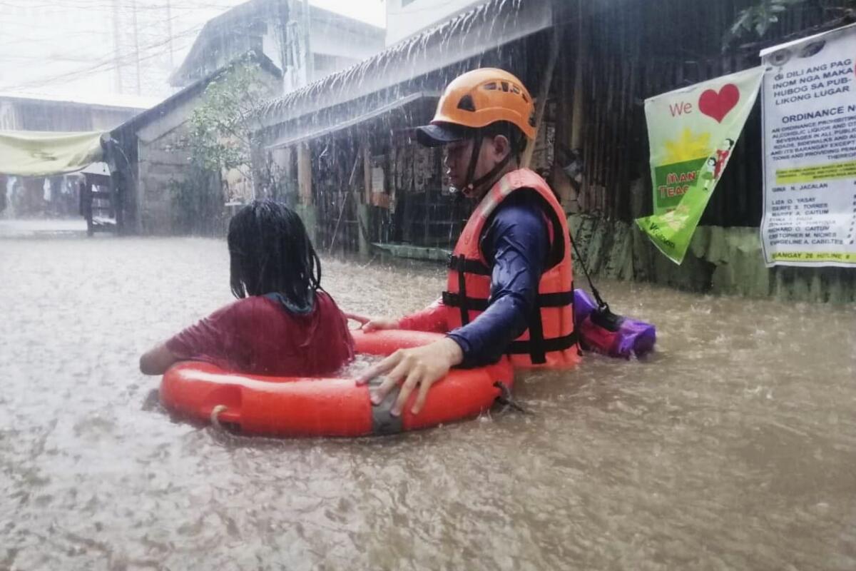 A helmeted man guides a child in a life preserver through deep floodwater.