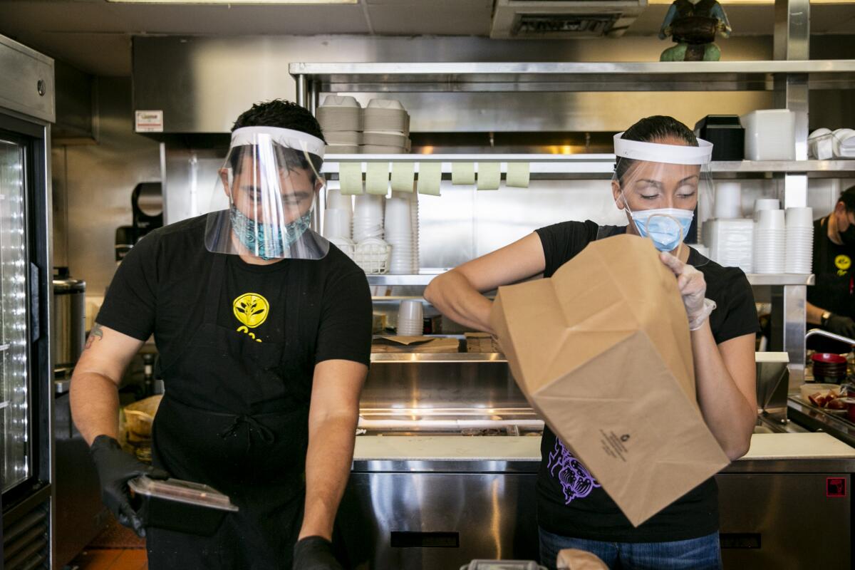 Two restaurant employees work while wearing face masks, face shields and gloves.