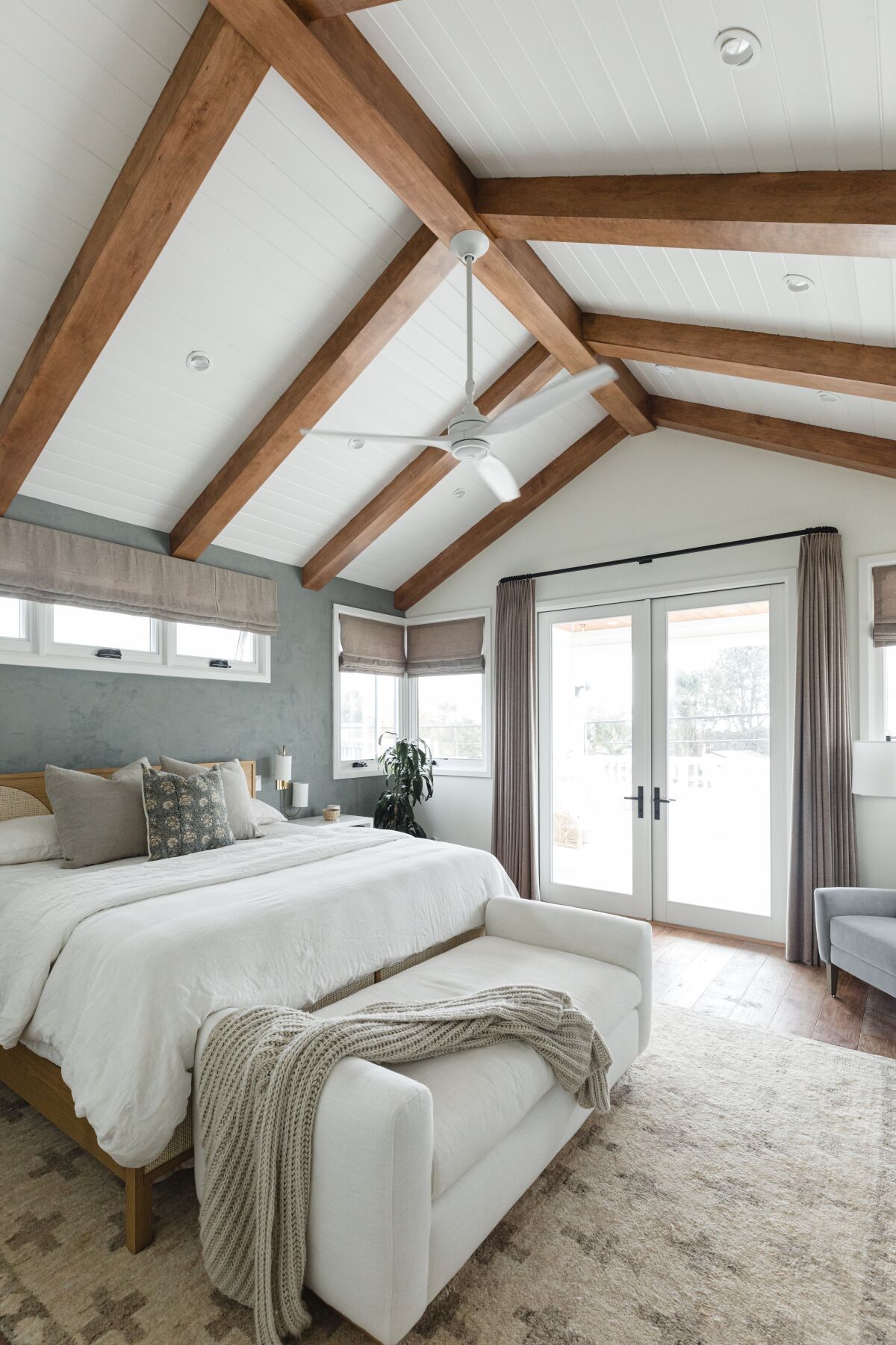 A spacious bedroom with a vaulted, wood-beam ceiling has organic materials, fabrics and colors throughout.