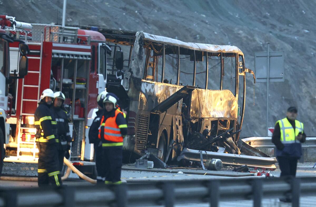 Emergency workers stand around the charred remains of a bus.