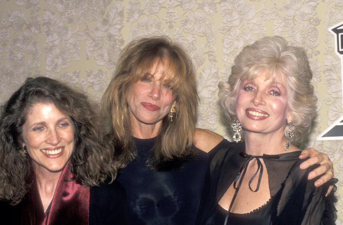 A woman wearing black stands in between two other women, with her arm around one of them