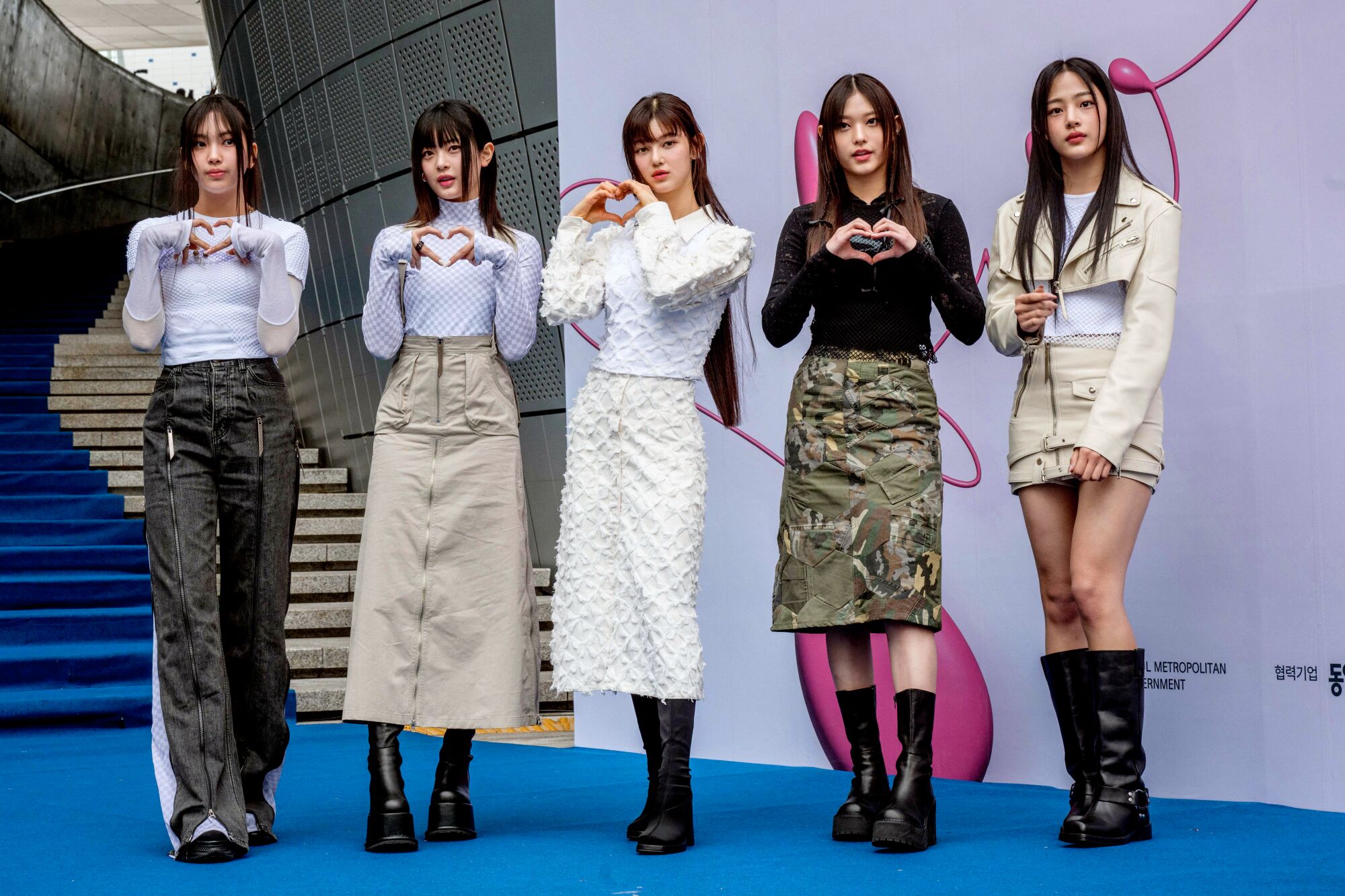 Five members of South Korean K-pop group New Jeans stand for a photo shoot with hands forming a heart