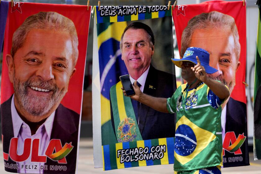 FILE - A demonstrator dressed in the colors of the Brazilian flag performs in front of a street vendor's towels for sale featuring Brazilian presidential candidates, current President Jair Bolsonaro, center, and former President Luiz Inacio Lula da Silva, in Brasilia, Brazil, Sept. 27, 2022. Brazil is days from a historic presidential election set for Oct. 30 featuring two political titans and bitter rivals that could usher in another four years of far-right politics or return a leftist to the nation’s top job. (AP Photo/Eraldo Peres, File)