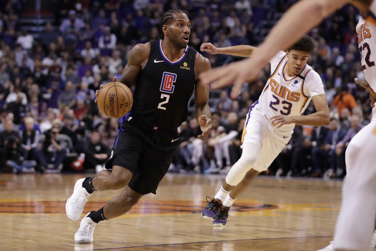 El pivot de los Clippers de Los Ángeles Kawhi Leonard avanza con el balón superando al pivot de los Suns de Phoenix Cameron Johnson en el juego del miércoles 26 de febrero del 2020.