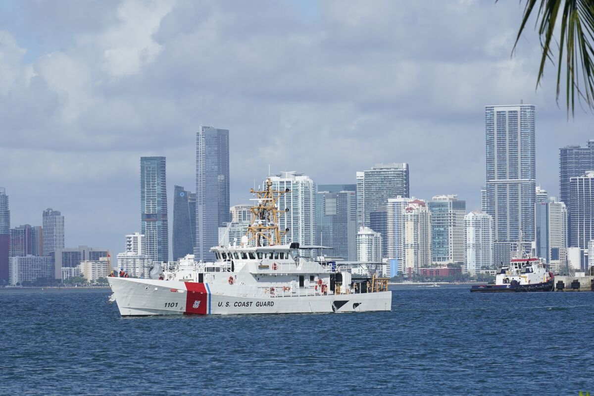 A white ship bearing the words U.S. Coast Guard is seen at sea against a backdrop of skyscrapers