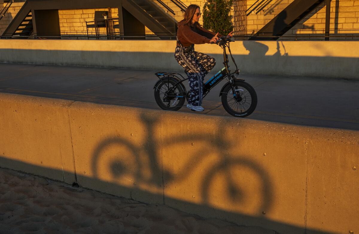 A woman riders her e-bike on the Strand in Hermosa Beach.