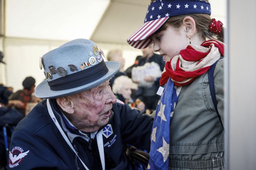 U.S. veteran SSgt. Jake M. Larson talks to a girl who wears an American flag around her neck during a gathering in preparation of the 79th D-Day anniversary in La Fiere, Normandy, France, Sunday, June 4, 2023. The landings on the coast of Normandy 79 year ago by U.S. and British troops took place on June 6, 1944. (AP Photo/Thomas Padilla)