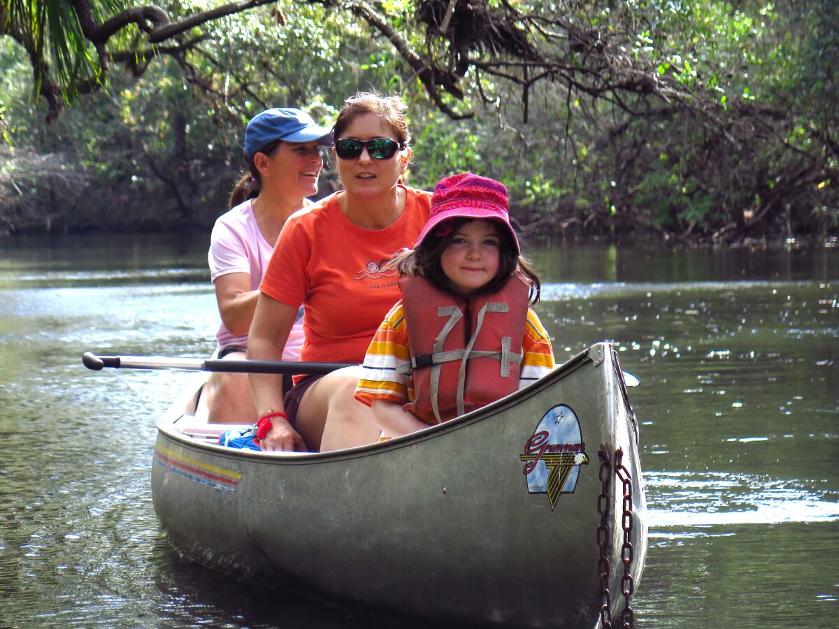A girl and two women ride in a canoe on a river.
