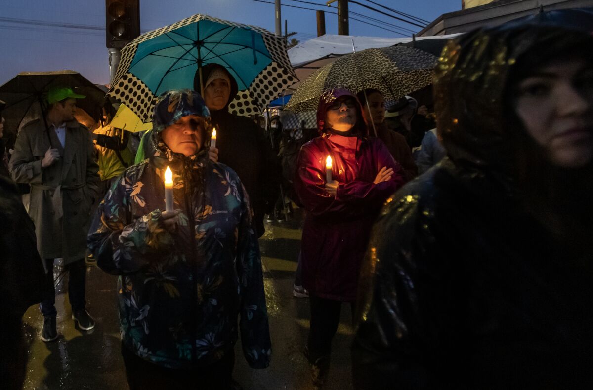People hold umbrellas and candles at a vigil.