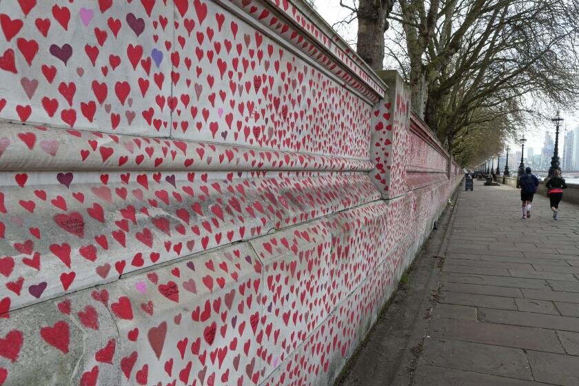 People jog past the 'The National COVID Memorial Wall' on the south bank of the Thames in front of St. Thomas' hospital and opposite the House of Parliament in London, Sunday April 4, 2021. Hearts are being drawn onto the wall in memory of the many thousands of people who have died in the UK from coronavirus, with organizers hoping to reach their target of 150,000 hearts by the middle of next week. (AP Photo/Tony Hicks)