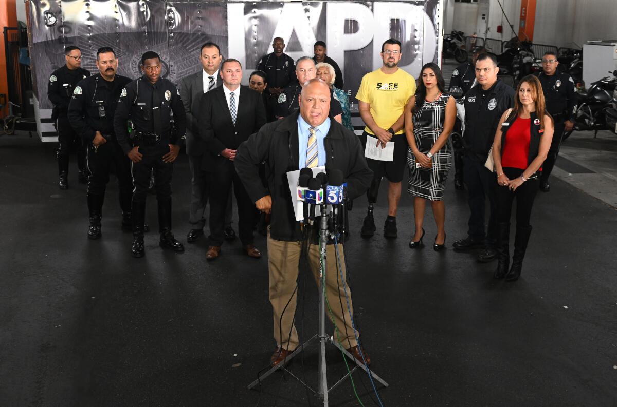 People stand behind LAPD Det. Ryan Moreno as he speaks during a news conference in Los Angeles.