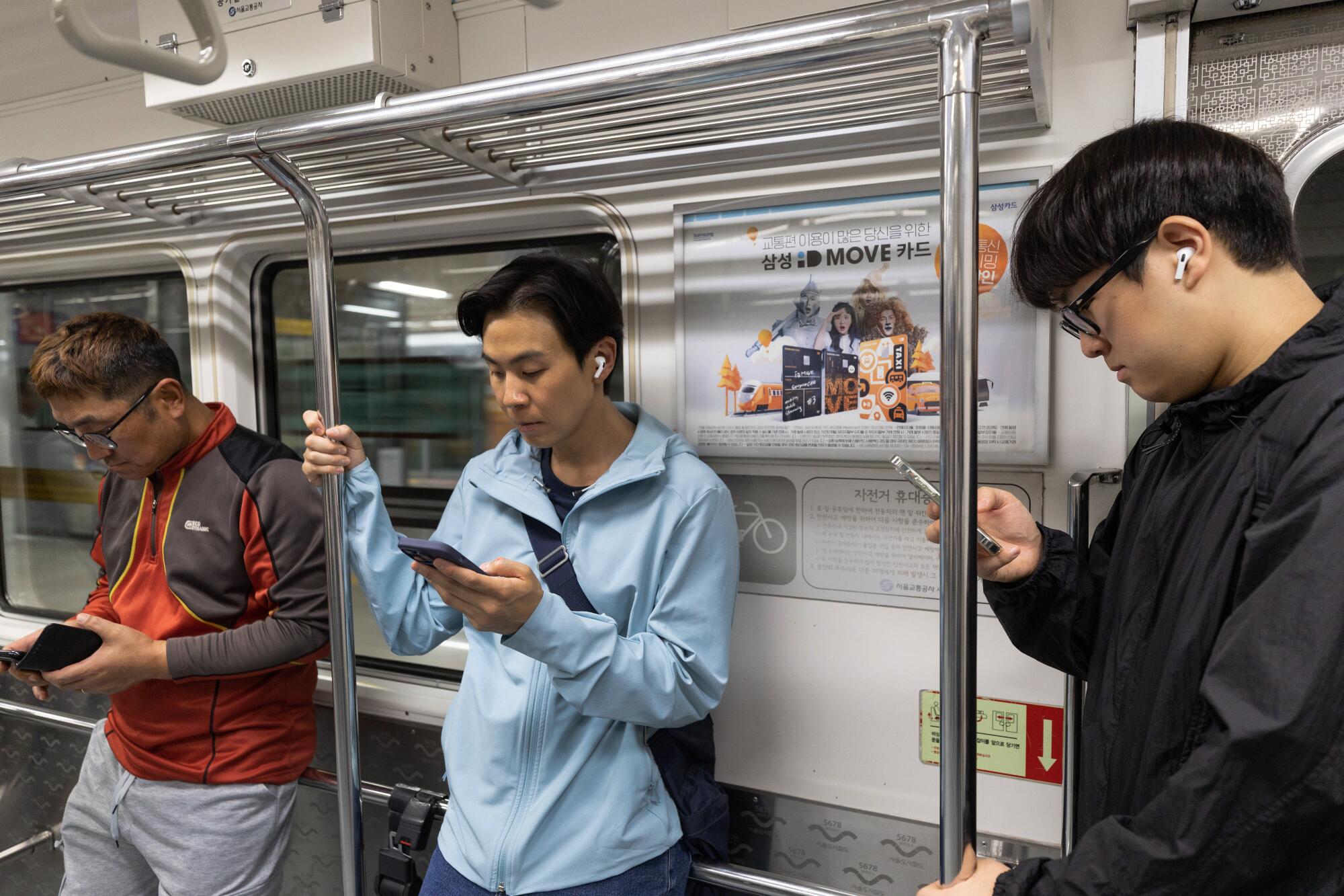 Three men stand looking at their phones in a subway car 