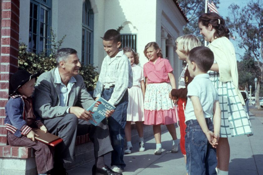 American author and illustrator Dr Seuss (Theodor Seuss Geisel, 1904 - 1991) sits outdoors talking with a group of children, holding a copy of his book, 'The Cat in the Hat', La Jolla, California, April 25, 1957. (Photo by Gene Lester/Getty Images)