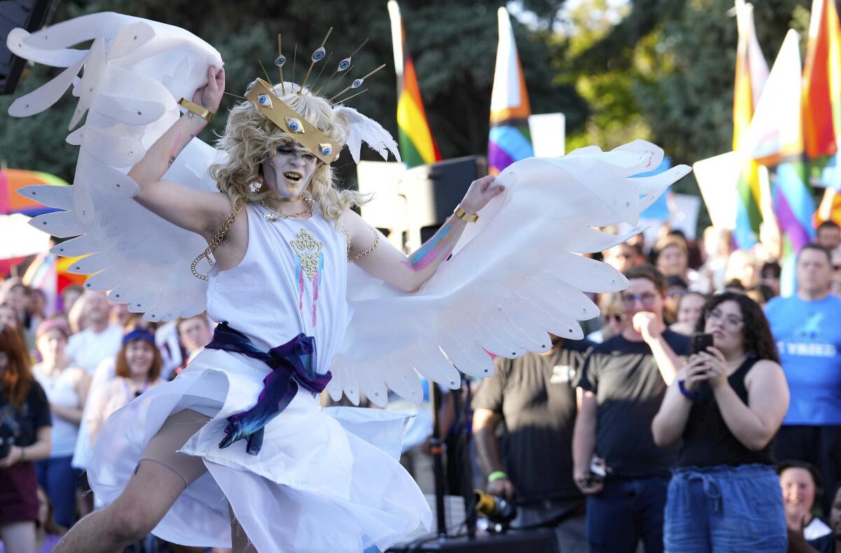 A drag performer raises white fabric wings during an outdoors show.