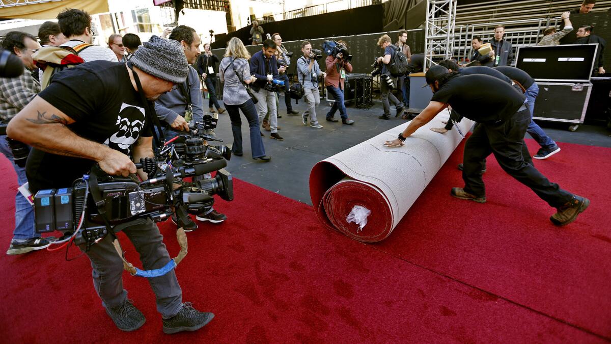 A cameraman films workers rolling out the red carpet. (Al Seib / Los Angeles Times)