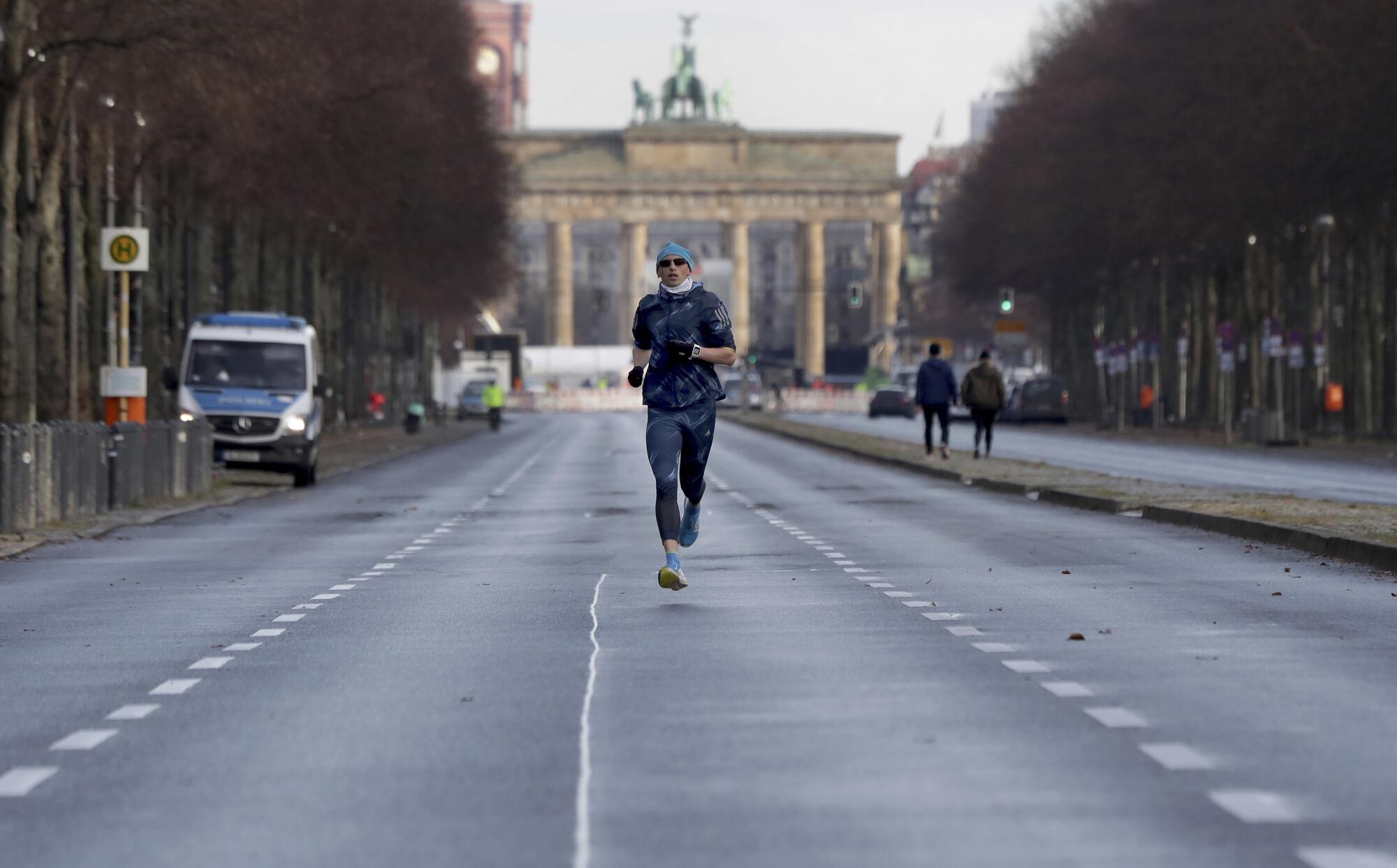 A man in beanie, sunglasses and mask jobs along an empty roadway in Berlin.
