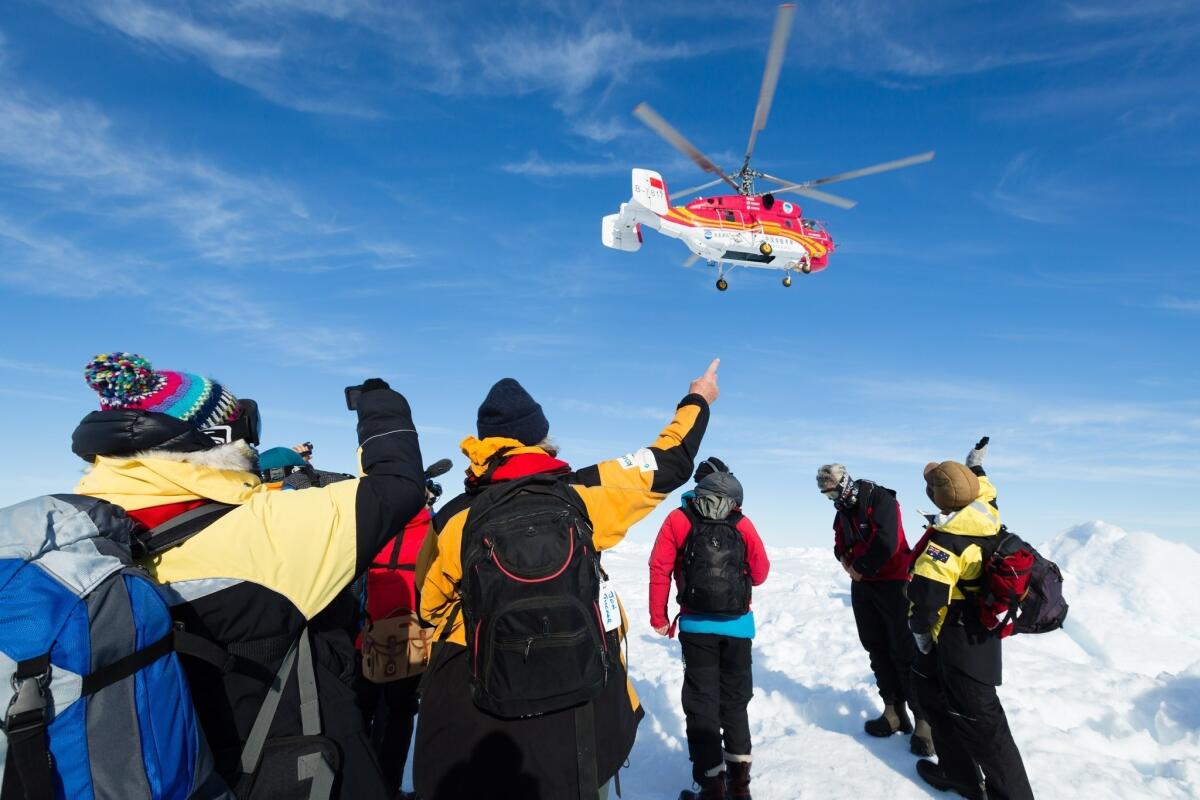 Passengers from the stranded Russian ship Akademik Shokalskiy watch a helicopter from the Chinese icebreaker Xue Long that has arrived to rescue them.