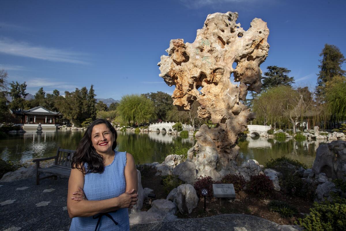 Cris Lutz, in a light blue dress, stands before a pond in the Huntington's Chinese garden