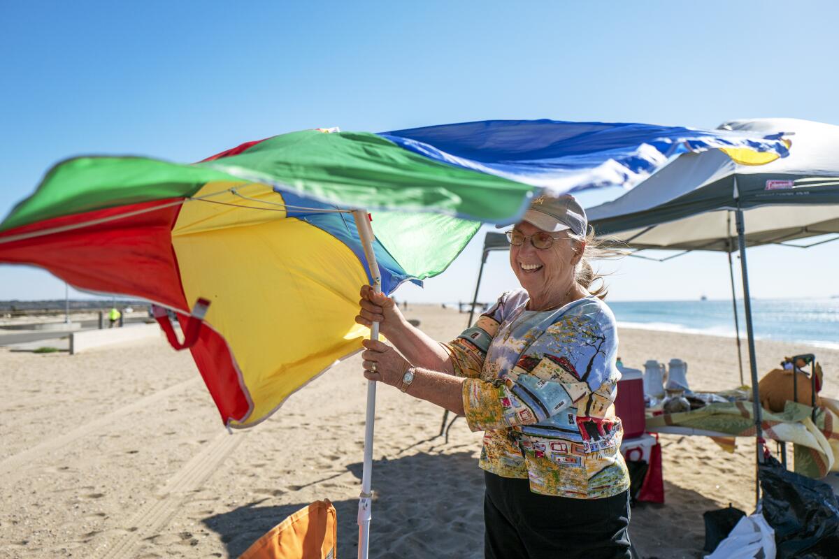 Sue West of Costa Mesa holds on to her umbrella as the winds kick up at Bolsa Chica State Beach in Huntington Beach.