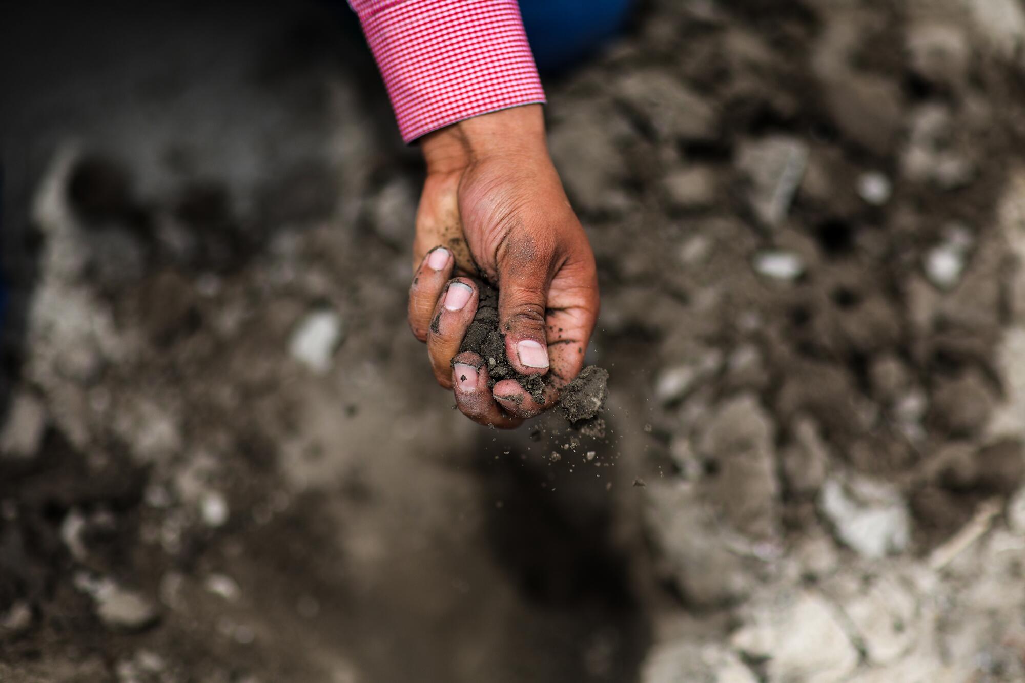A hand squeezes dirt to check its moisture content 