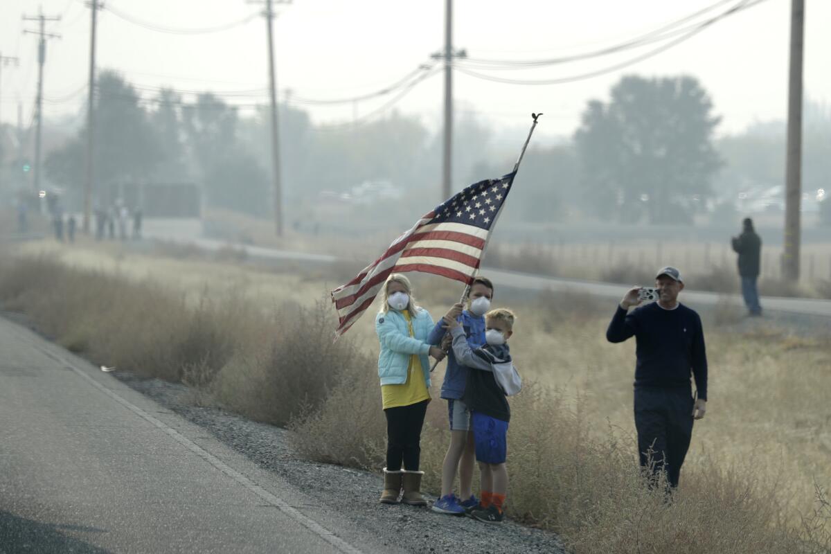 People wearing face masks and holding an American flag await President Trump's motorcade in Chico.