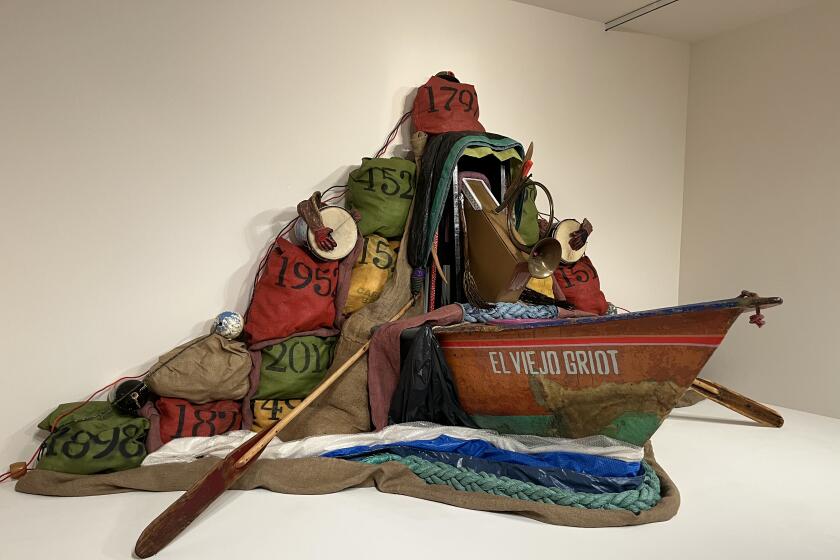An assemblage features the prow of a boat emerging from a gallery wall, surrounded by tarps and rope to evoke water